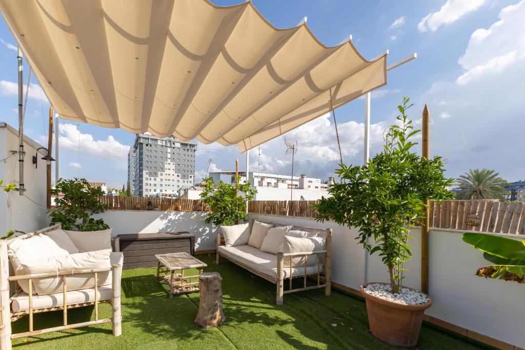 un patio con sofá y sillas bajo una sombrilla grande en Tentudia Charming Apartments with Private Roof-Top or Patio in San Bernardo By Oui Seville en Sevilla