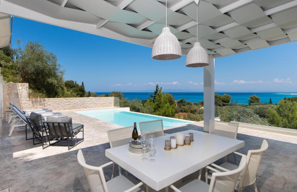a patio with a white table and chairs and a swimming pool at Villa Anthos - Fresh modern villa, pool, close to the beach in Lefkada Town
