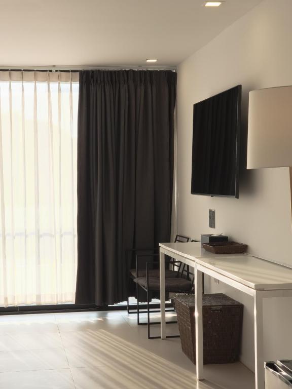 A wall-mounted television and narrow writing desk beside a bright window.
