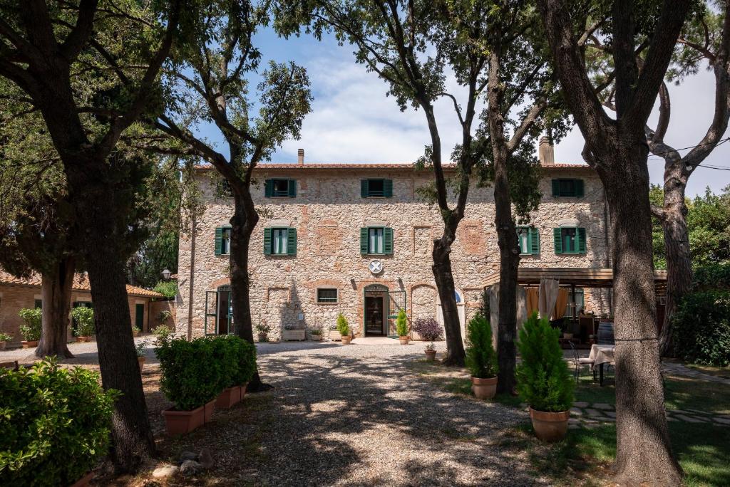 una vieja casa de piedra con árboles delante de ella en Razza del Casalone, en Grosseto