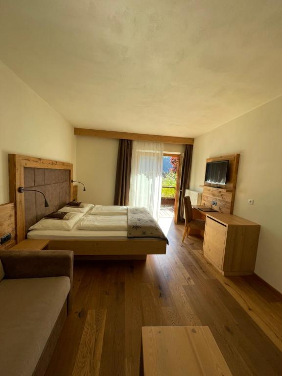 een slaapkamer met een bed, een bank en een televisie bij Pension Moarhof in Feldthurns