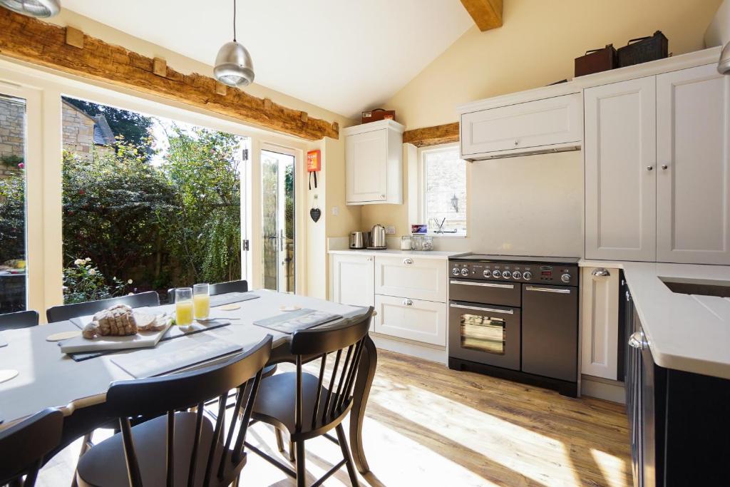 una cocina con armarios blancos y una mesa con sillas. en Grooms Lodge, Chipping Campden - Taswell Retreats, en Chipping Campden