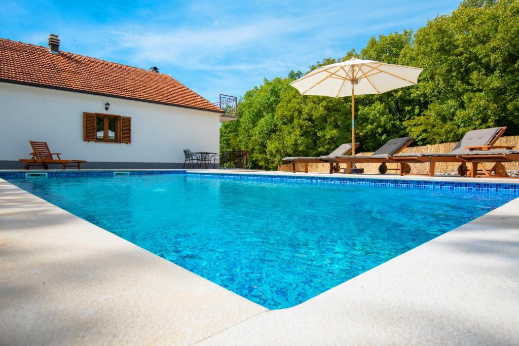 a swimming pool with an umbrella and chairs and a house at Holiday House Tone, Imotski-Drum-Makarska in Drum
