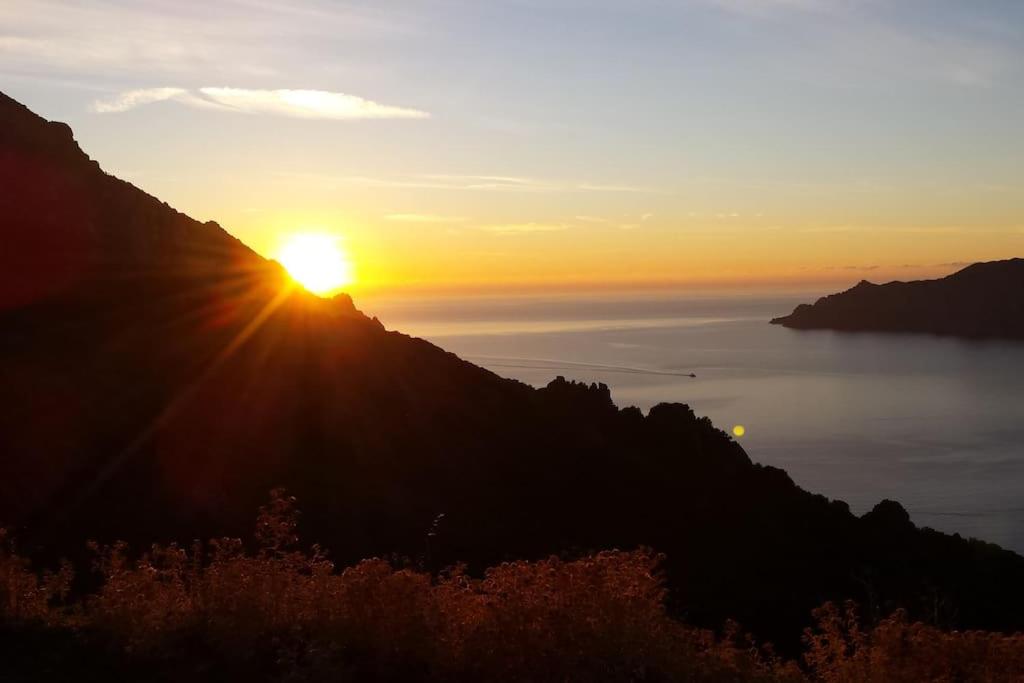 a sunset on a mountain with the sun setting over the ocean at studio terremer in Patrimonio