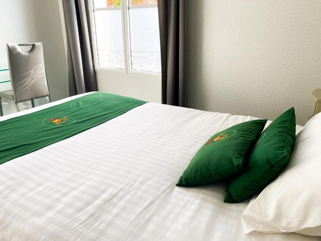 a white bed with two green pillows on it at Colette Hôtel in Niort