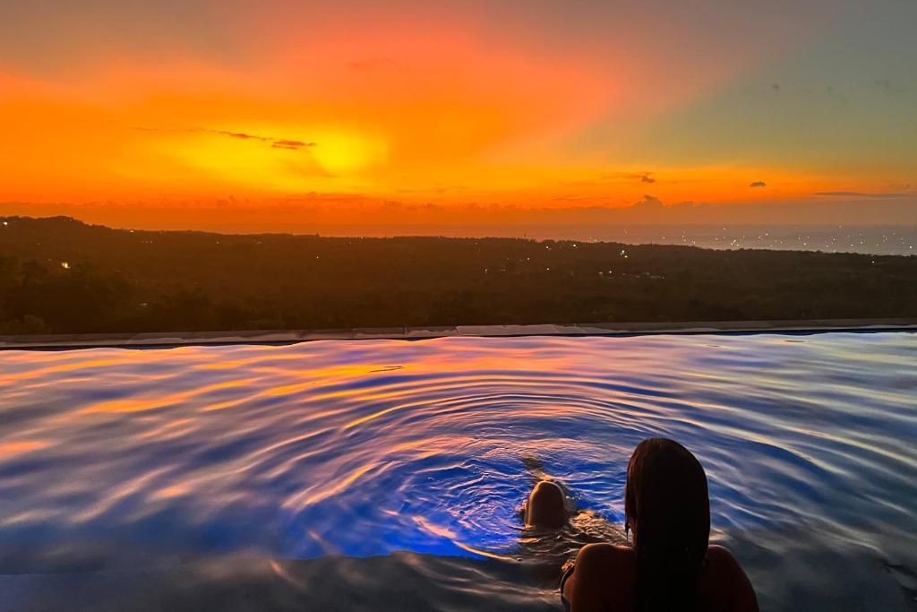 a woman sitting in a pool at sunset at Uluwatu Sunset Hills in Uluwatu