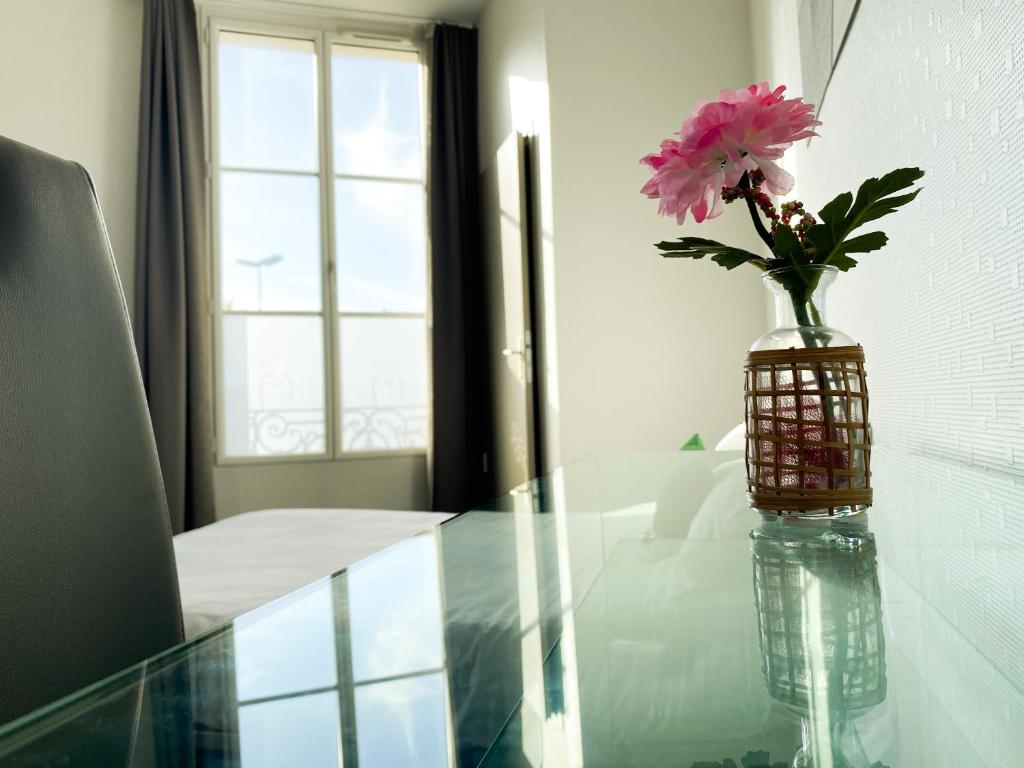 a vase with a pink flower sitting on a glass table at Colette Hôtel in Niort