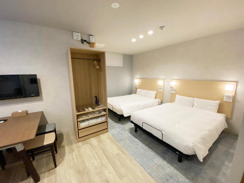 広島市にあるたかのばしホテルのベッド2台、デスク、テレビが備わるホテルルームです。