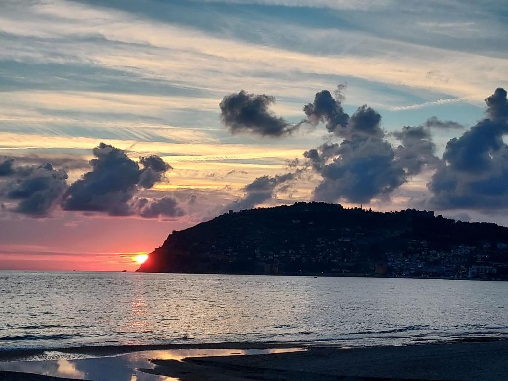 a sunset over the ocean with a hill in the background at Larsens Suit Hotel in Alanya