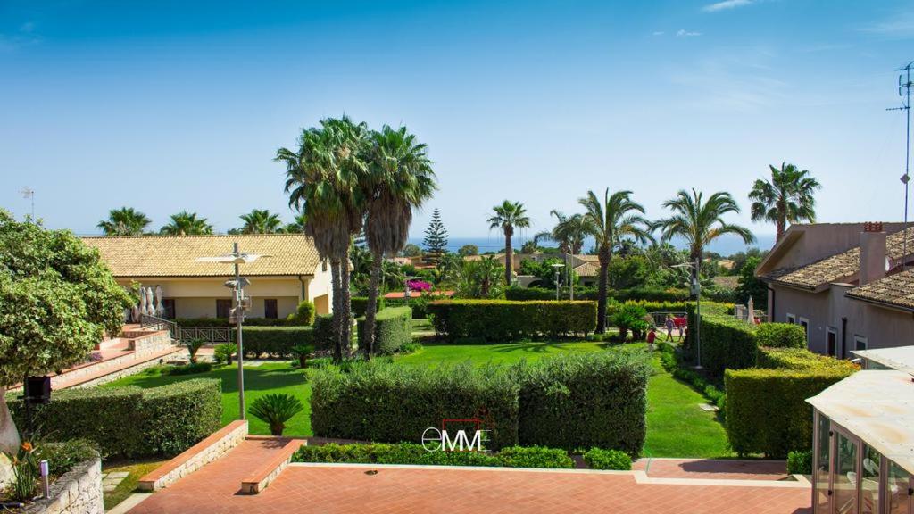 Blick auf einen Garten mit Palmen und ein Haus in der Unterkunft Hotel La Cavalera in Augusta