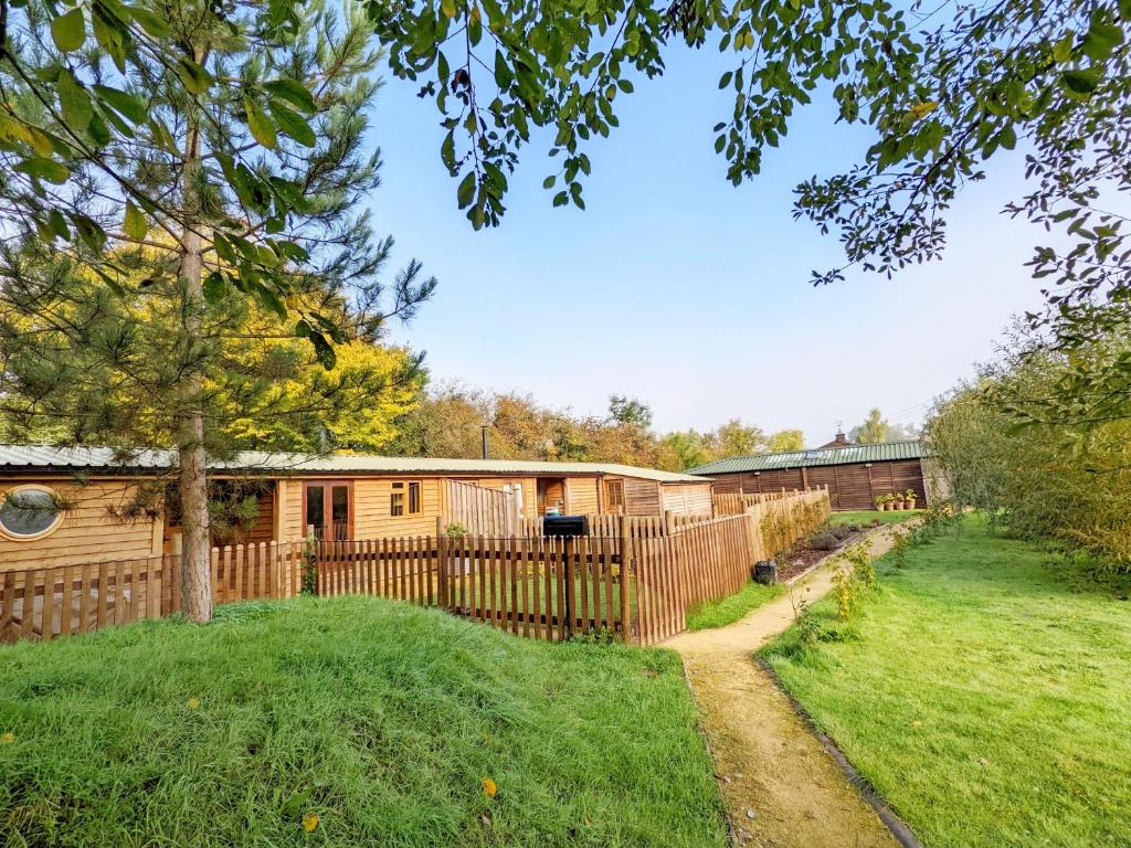 uma casa de madeira com uma cerca e um quintal em The Quail Cabin em Kirdford