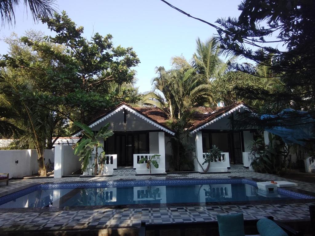 a swimming pool in front of a house with trees at God's Gift Morjim in Morjim