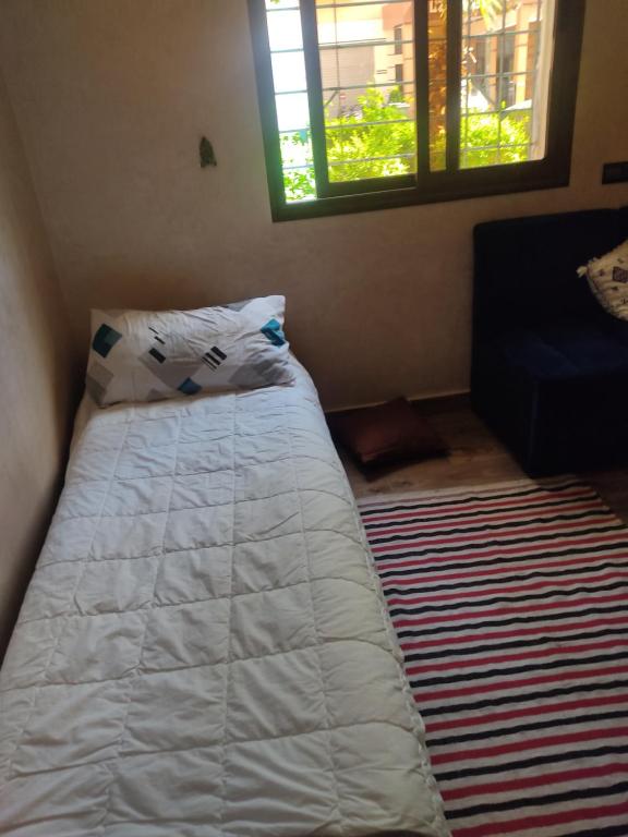 um quarto com uma cama com lençóis brancos e uma janela em Joli Appartement au portes de Marrakech 