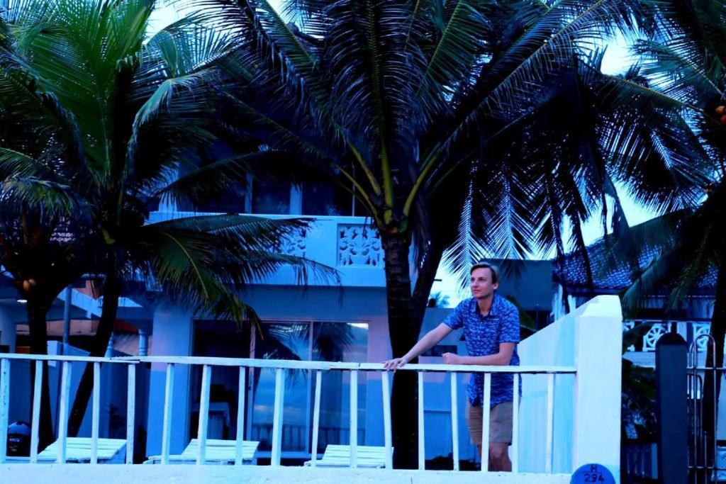 a woman sitting on a railing next to palm trees at Shenora Beach Resort in Hikkaduwa