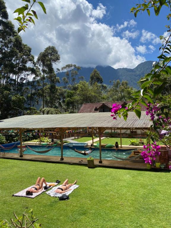 two people laying on the grass near a swimming pool at Mama Tungu hostel in Baños