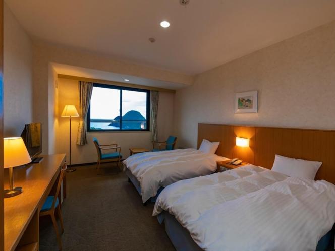 um quarto de hotel com duas camas e uma secretária em Kyukamura Takeno-Kaigan em Toyooka