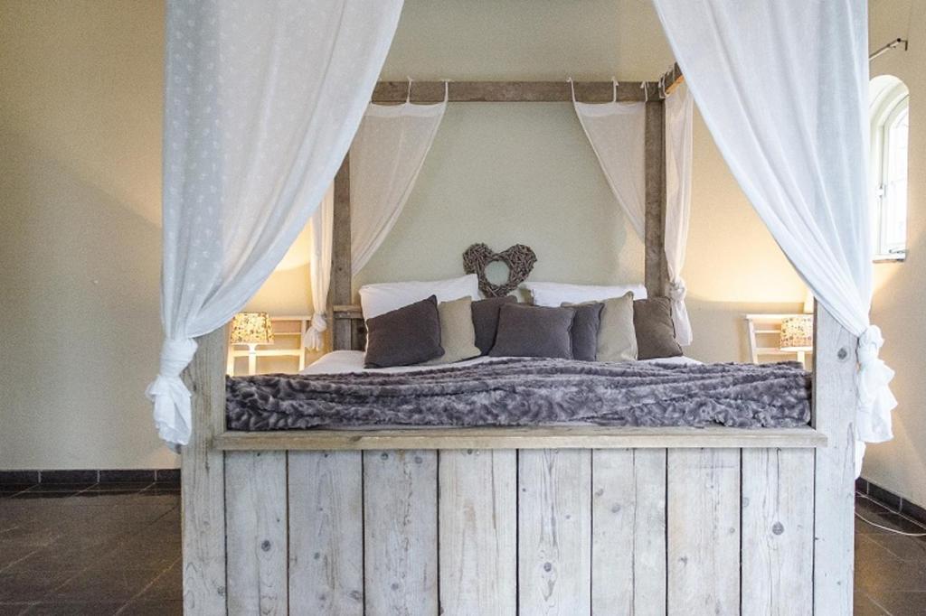 een slaapkamer met een hemelbed met gordijnen en kussens bij B&B de Remketting in Slijk-Ewijk