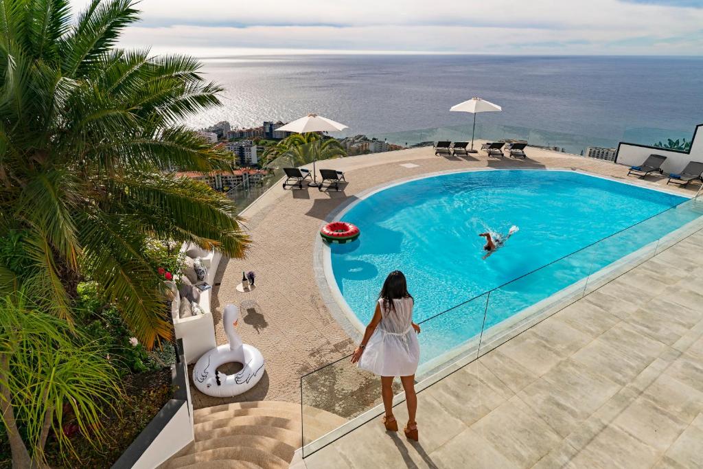 een vrouw op een balkon met uitzicht op een zwembad bij Sky Villa by An Island Apart in Funchal