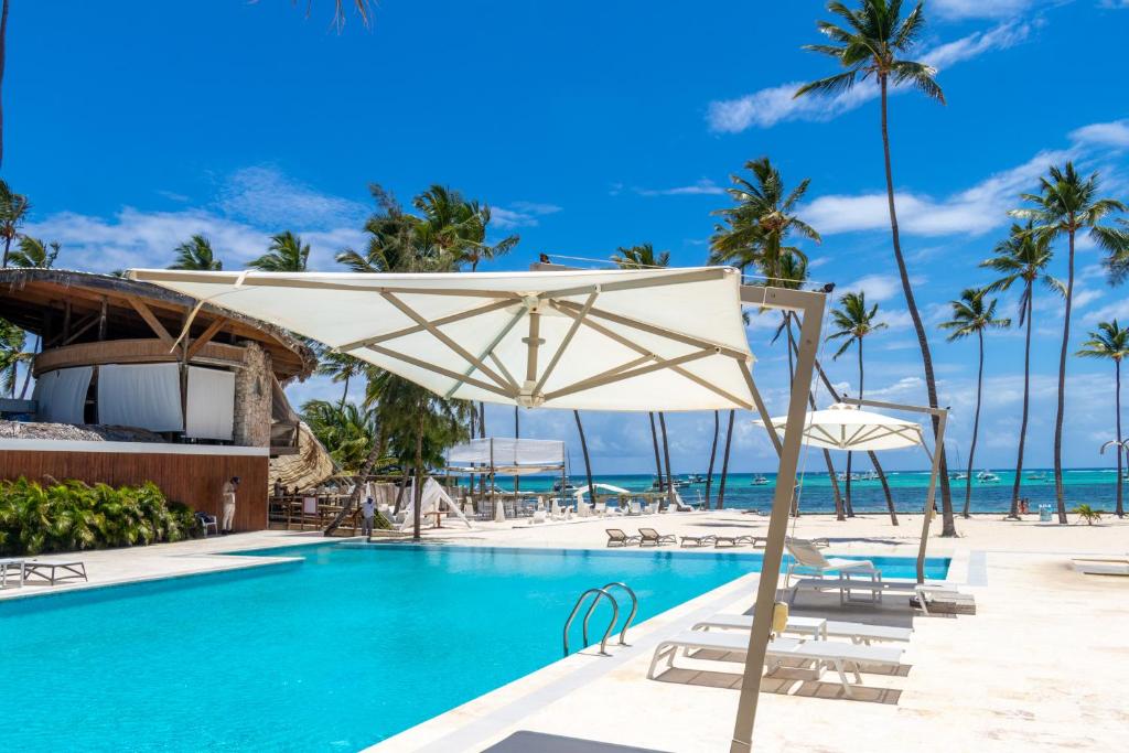 a pool with chairs and umbrellas next to the ocean at Family Getaway Apartment - Right On The Beach in Punta Cana