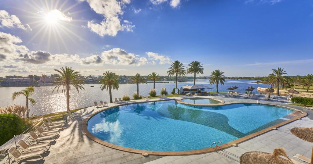 a large swimming pool next to a body of water at BelleVue Club in Port d'Alcudia