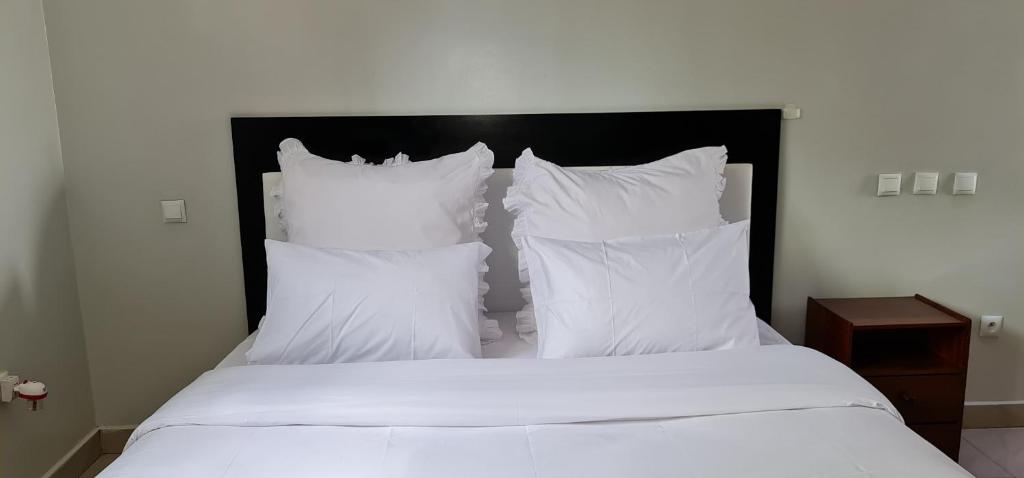Cama con sábanas y almohadas blancas en Traveller's StaY, en Kigali