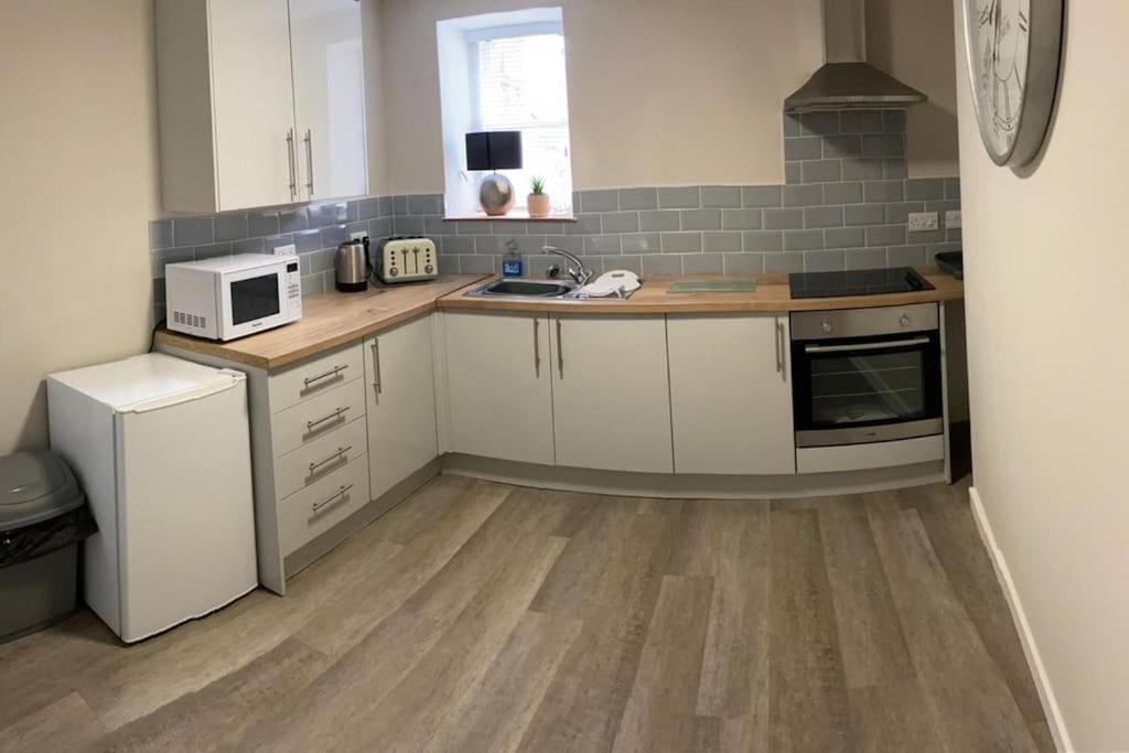 a kitchen with white cabinets and a sink and a microwave at Siop Iwan a Menna in Caernarfon