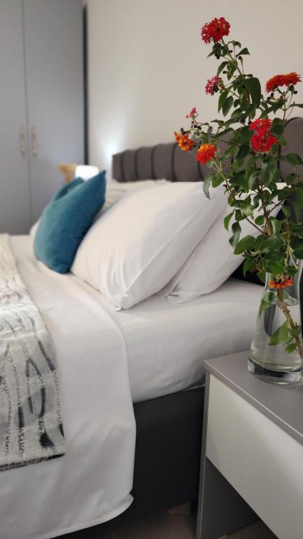 Una cama con sábanas blancas y un jarrón con flores rojas. en Divjaka Apartments 2 - City Center, en Divjakë