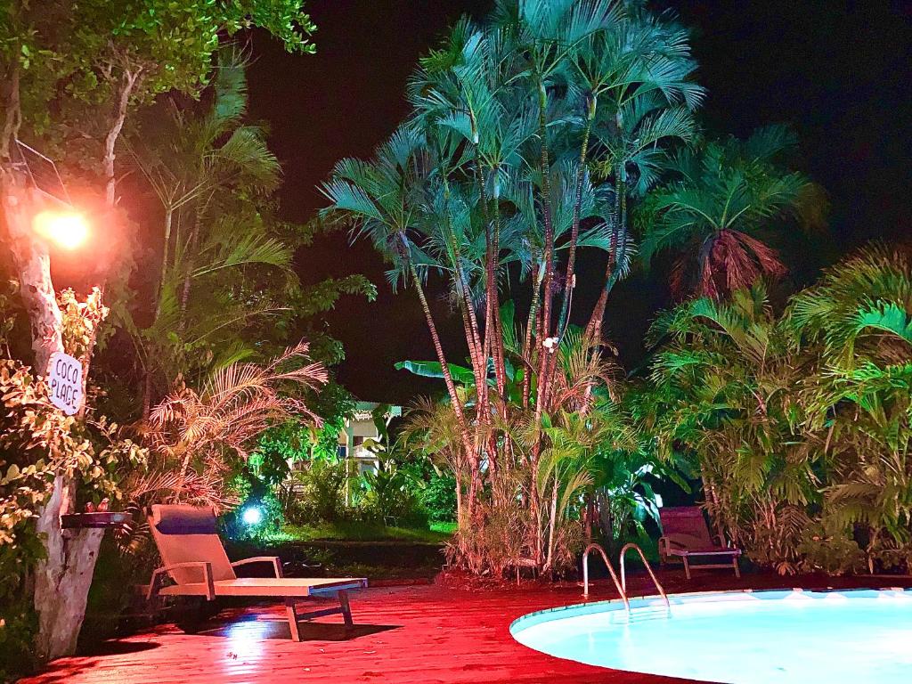 LODGE PAMPLEMOUSSE avec PISCINE privative , dans parc calme à 500 m plage في لو كاربيت: وجود مسبح والكراسي والنخيل في الليل