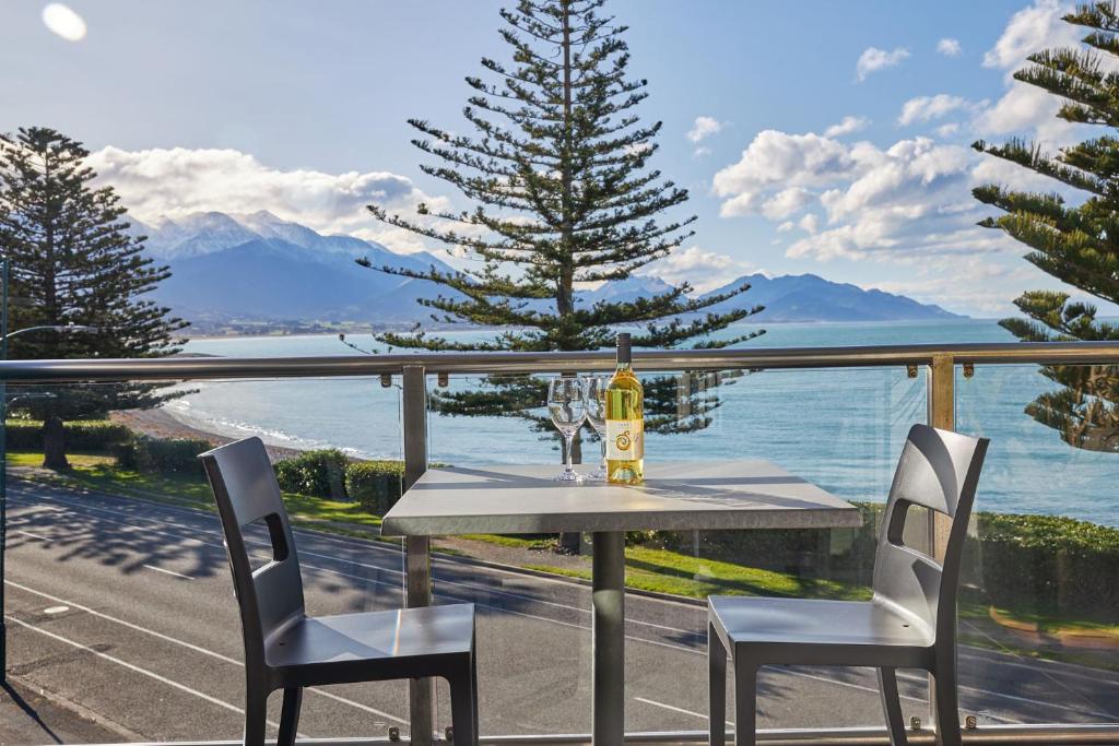 een tafel met een fles wijn en 2 stoelen op een balkon bij Waves on the Esplanade in Kaikoura