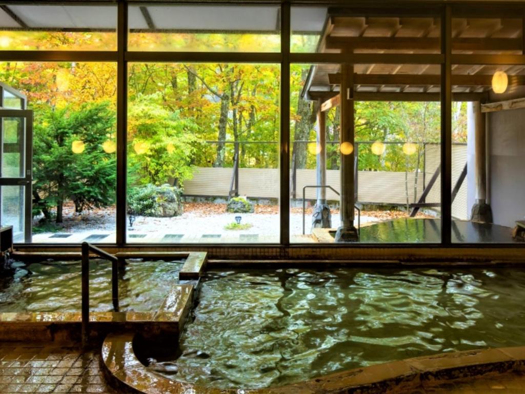 una gran piscina de agua en una habitación con ventanas en Kyukamura Tsumagoi-Kazawa, en Tsumagoi
