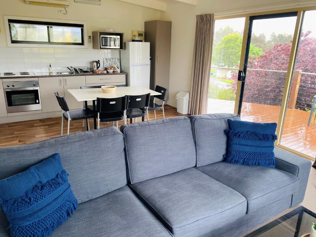 a living room with a blue couch and a kitchen at Cedar Apartments - Merrijig in Merrijig