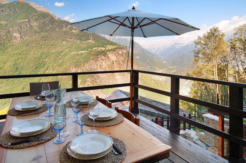 a wooden table with glasses and an umbrella on a balcony at Sweet Somma Mountain Lodge 2 in San Guglielmo