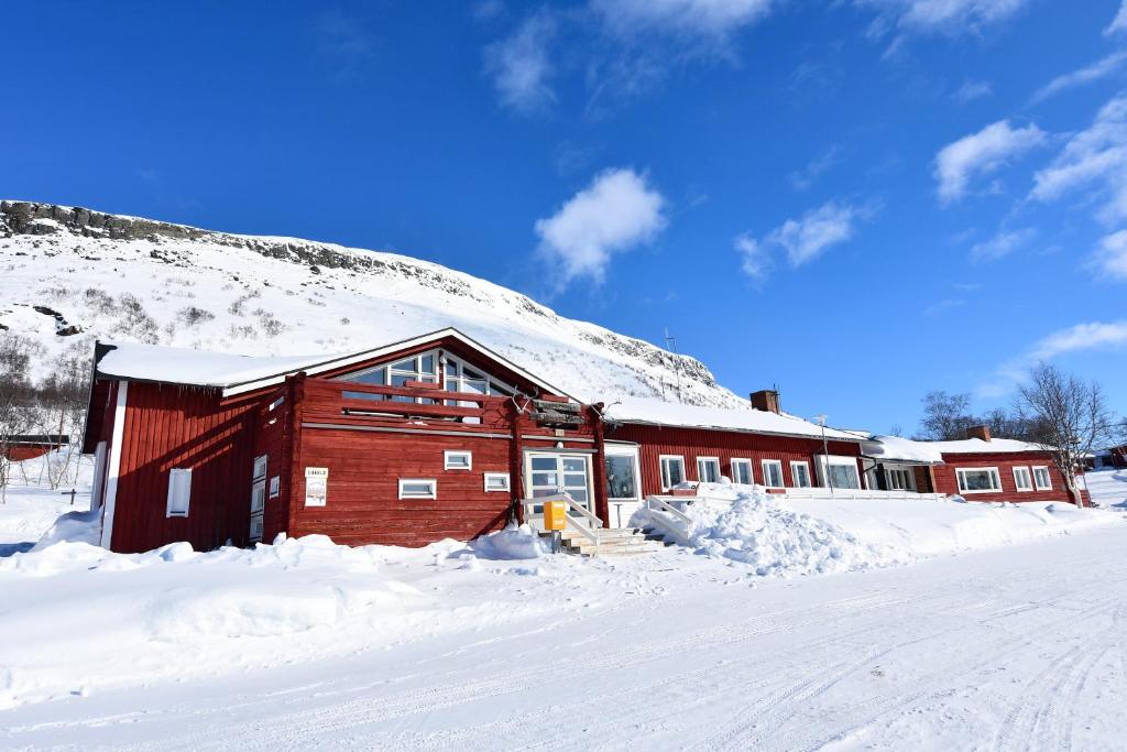 a red building in the snow with a snow covered hill at Kilpisjärven Retkeilykeskus Rooms in Kilpisjärvi