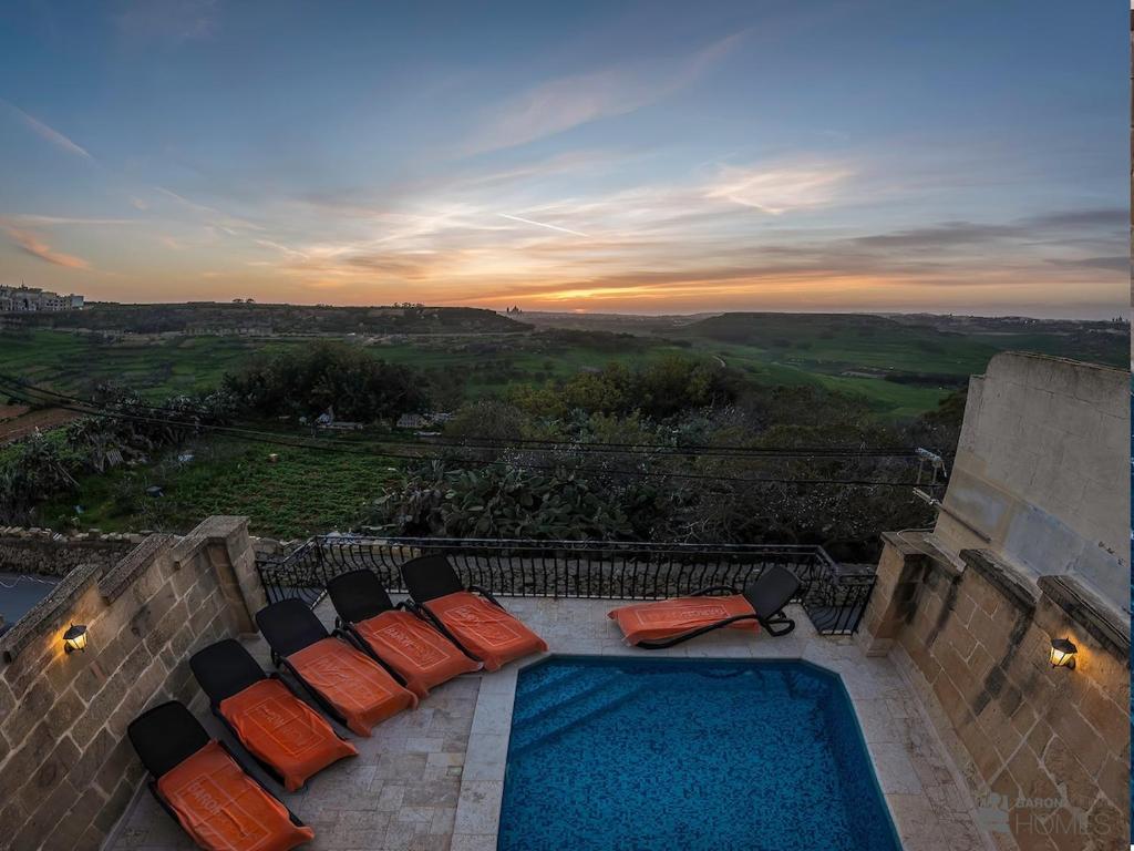 a patio with chairs and a swimming pool at sunset at Ta Rena Holiday Home in Nadur