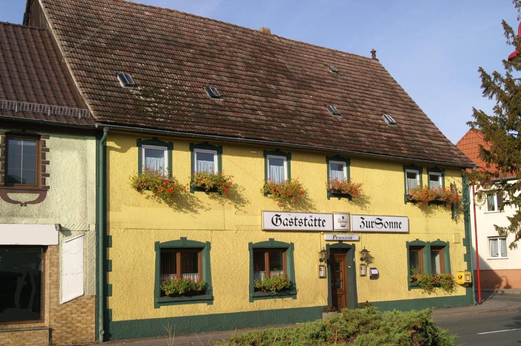 ein gelbes Gebäude mit Blumenkästen an den Fenstern in der Unterkunft Pension Zur Sonne in Mansfeld