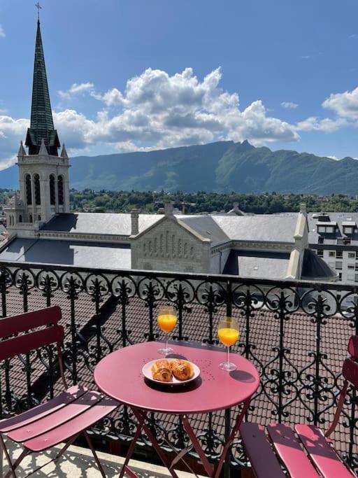 une table rose avec deux verres sur un balcon avec une église dans l'établissement Studio cosy, hyper centre d'Aix, vue montagnes, proche thermes, à Aix-les-Bains