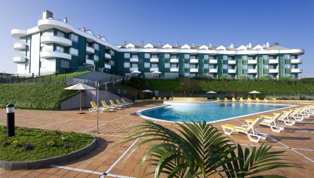 a hotel with a swimming pool and chairs and a building at Playas de Liencres - Hotel & Apartamentos in Boó de Piélagos