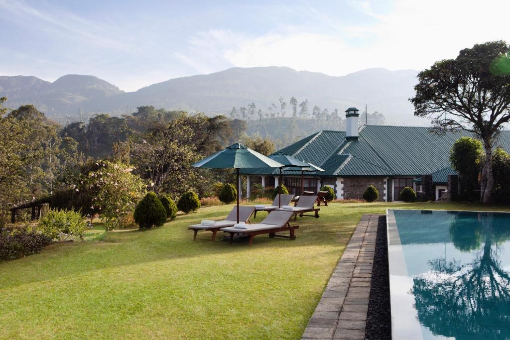 a house with a swimming pool with chairs and an umbrella at Ceylon Tea Trails in Hatton