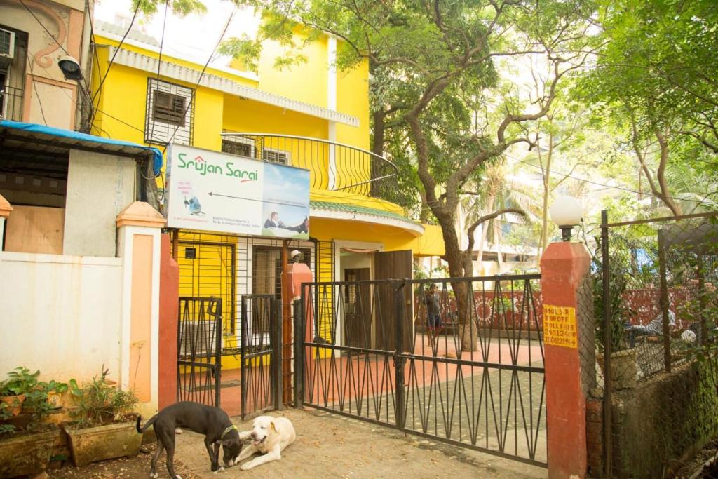 ムンバイにあるSrujan Sarai Service Apartmentの建物前の柵の横に立つ犬2匹