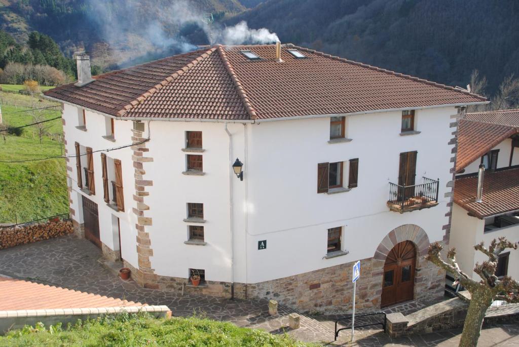 uma grande casa branca com uma montanha ao fundo em Matxitxulo Family Rooms em Ezkurra