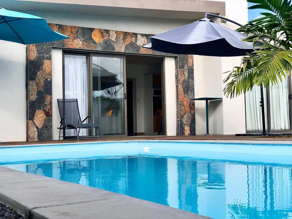 a swimming pool with an umbrella and a house at Sunny Side Up in Grand Baie