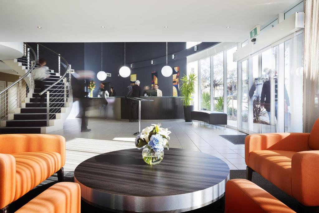 un vestíbulo con mesa y sillas naranjas en Ramada Encore Belconnen en Canberra