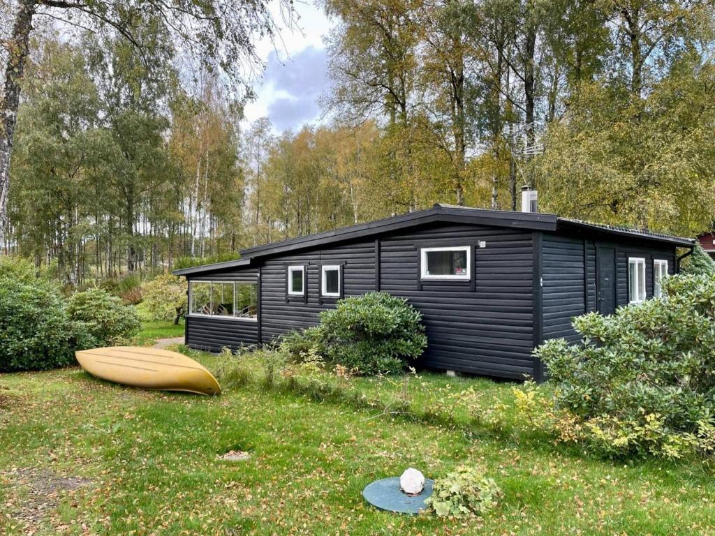 a black cabin with a surfboard in the grass at Holiday home HJÄRNARP II in Hjärnarp