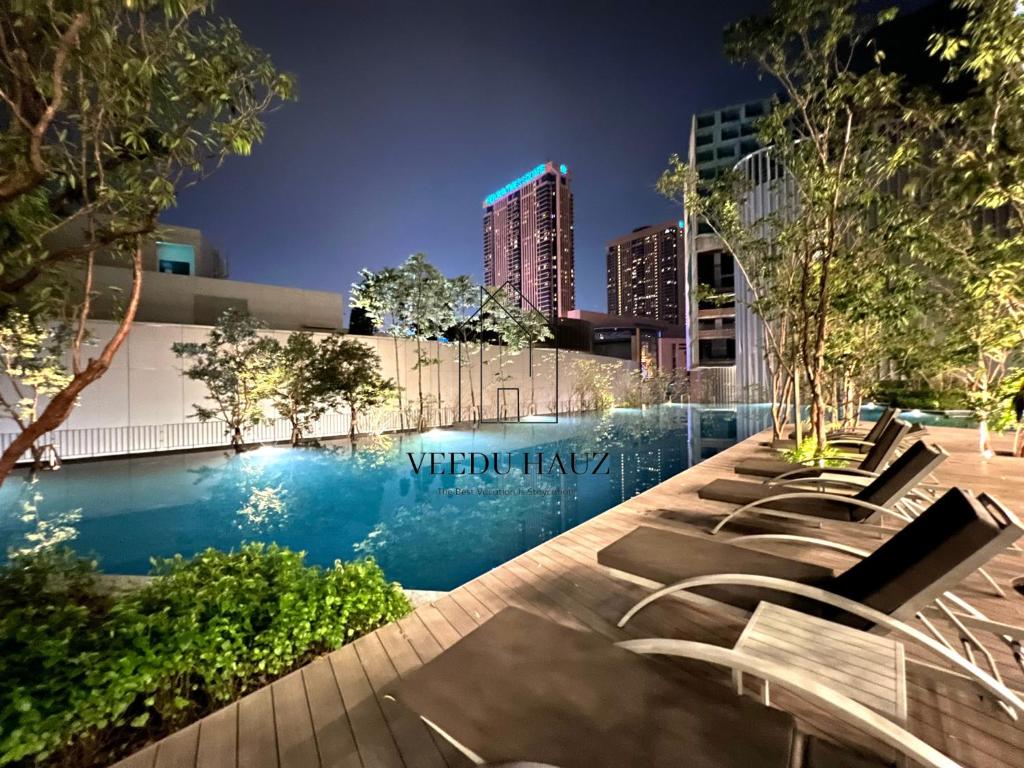 a pool with lounge chairs in a city at night at Lucentia Residences BBCC at Lalaport Kuala Lumpur by Veedu Hauz in Kuala Lumpur