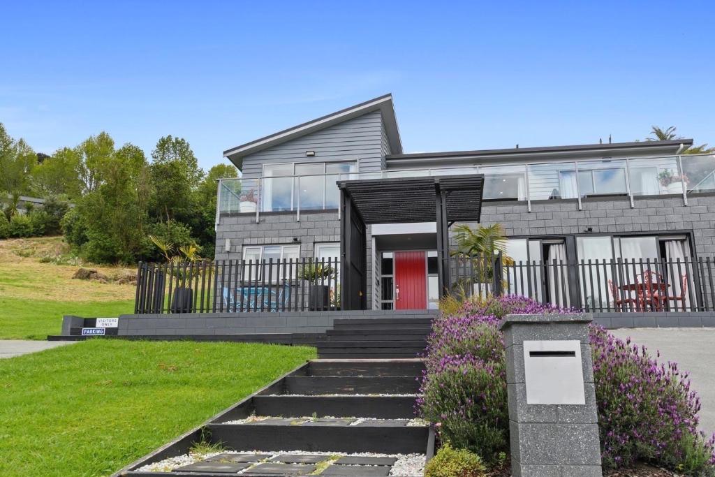 a gray house with a red door and some flowers at Mandeno Magic - Kerikeri Holiday Home in Kerikeri