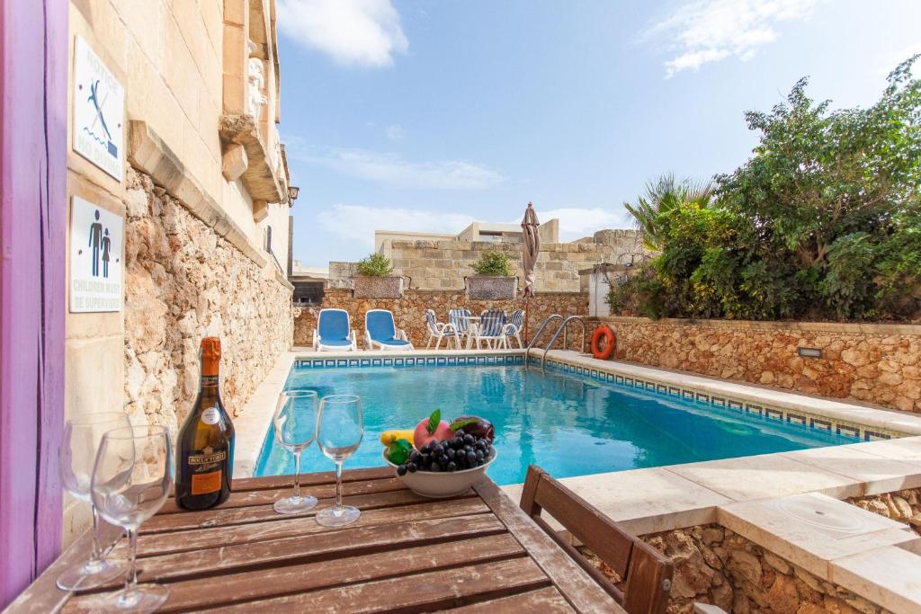 een zwembad met een tafel met wijnglazen en een fruitschaal bij Gozitan Farmhouse with Pool - PP 1 in Il-Wilġa