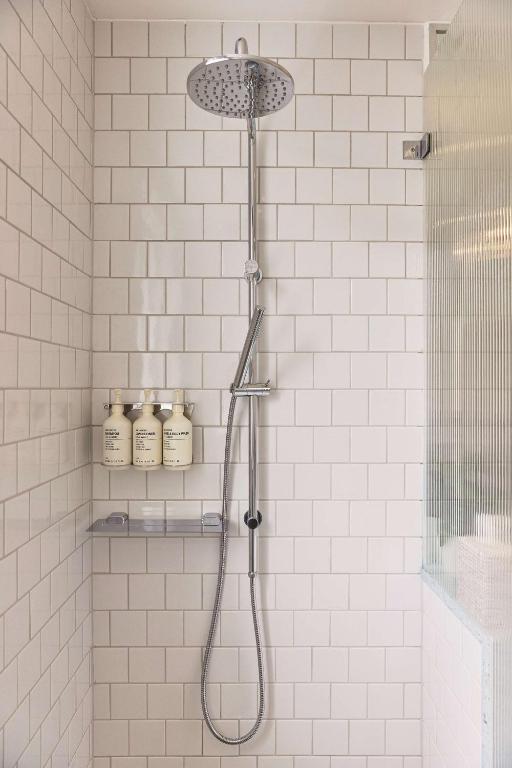a shower with a shower head in a white tiled bathroom at Adina Apartment Hotel Chippendale in Sydney