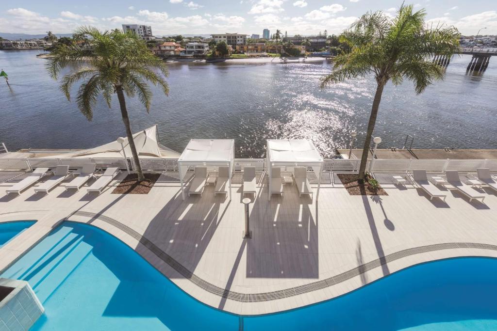 a pool with chairs and palm trees next to the water at Vibe Hotel Gold Coast in Gold Coast
