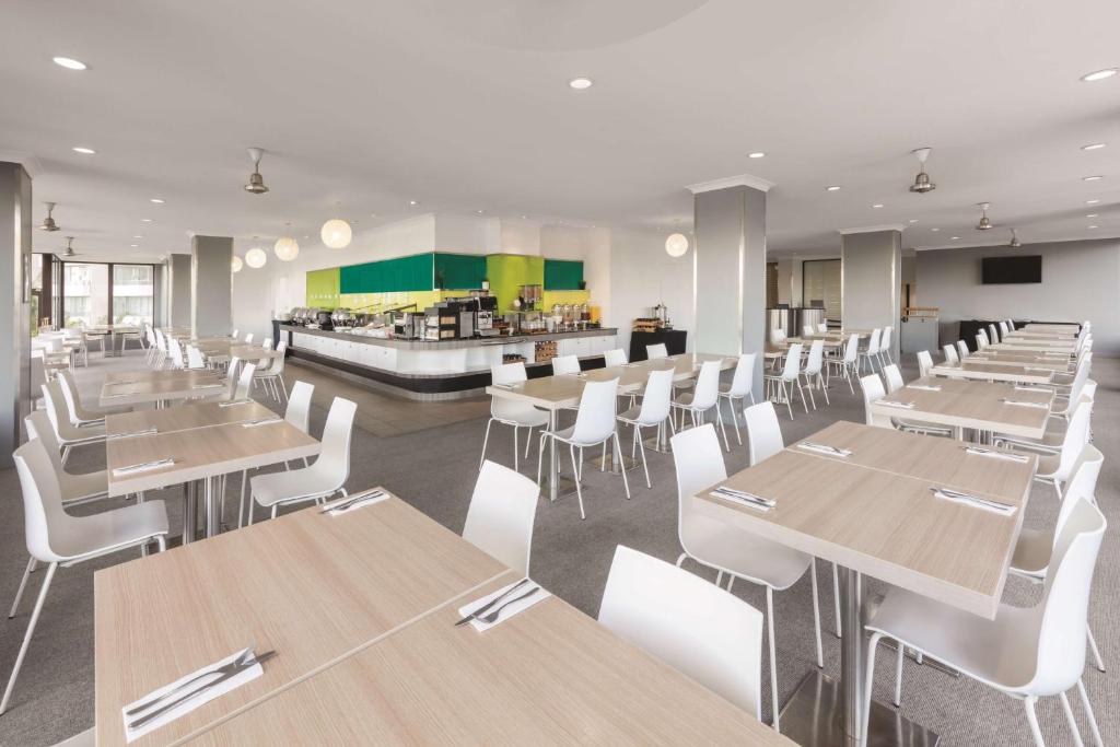 a restaurant with wooden tables and white chairs at Vibe Hotel Gold Coast in Gold Coast