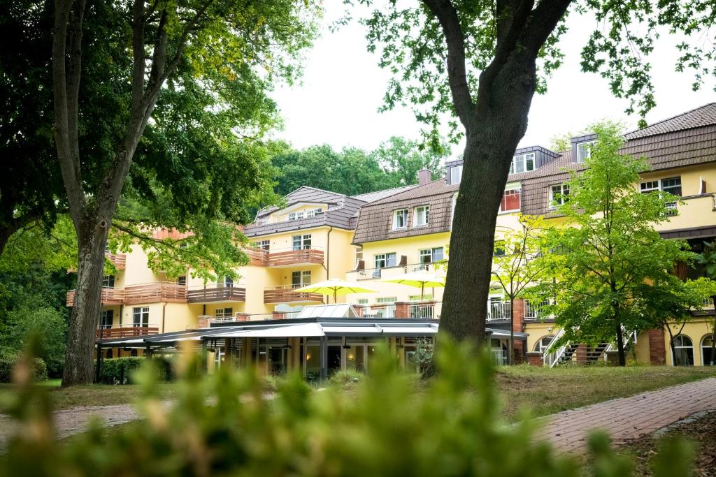 ein gelbes Gebäude mit Bäumen davor in der Unterkunft Kurhaus am Inselsee in Güstrow